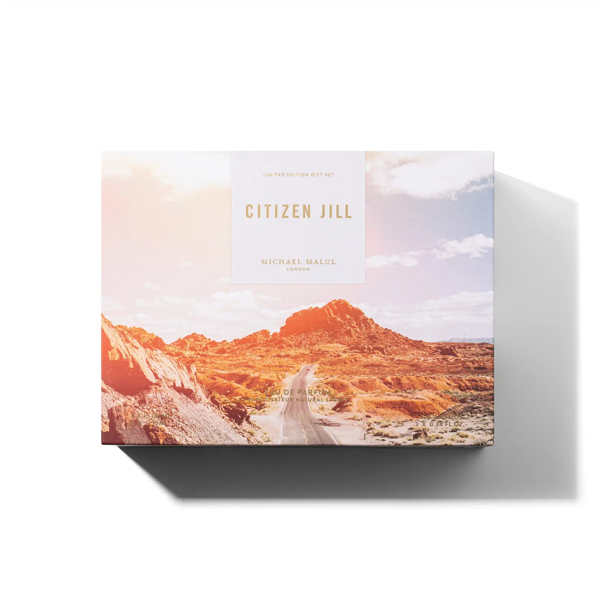 The MICHAEL MALUL CITIZEN JILL EDP WOMEN SET comes in a rectangular gift box with a desert landscape design featuring rocky hills and a dirt road under partly cloudy skies. The 3.4oz set casts a shadow to the right on a white background.