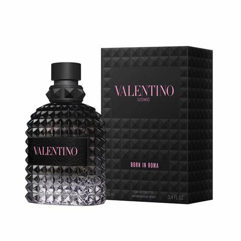 A clear, textured glass bottle of VALENTINO BORN IN ROME UOMO EDT MAN sits beside its matching black, patterned box with pink and white text. The VALENTINO mens fragrance features a black cap and a black label with Valentino in bright pink letters.