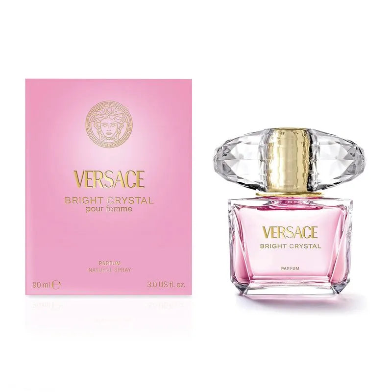 The VERSACE BRIGHT CRYSTAL PARFUM WOMEN bottle, adorned with a clear gem-like cap, sits beside its pink and gold box with gold Versace branding. Experience the pure parfum and radiant floral scent from VERSACE.